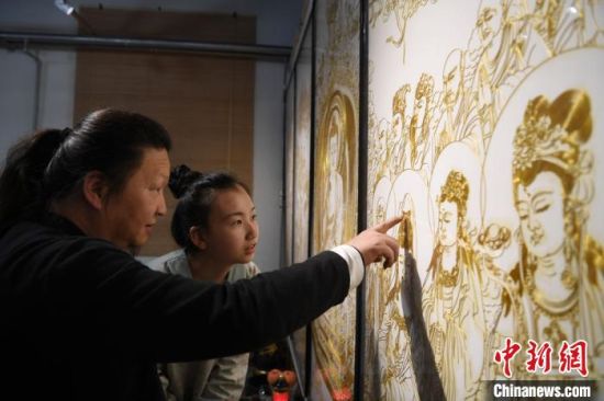 该画取材《灵山说法图》,内容涉及人物95个、瑞兽2只,掐丝勾勒出的人物神态、服饰、动作等栩栩如生。图为李海明正在给女儿李婕讲解其中的手艺精髓。 杨艳敏 摄 该画取材《灵山说法图》,内容涉及人物95个、瑞兽2只,掐丝勾勒出的人物神态、服饰、动作等栩栩如生。图为李海明正在给女儿李婕讲解其中的手艺精髓。 杨艳敏 摄